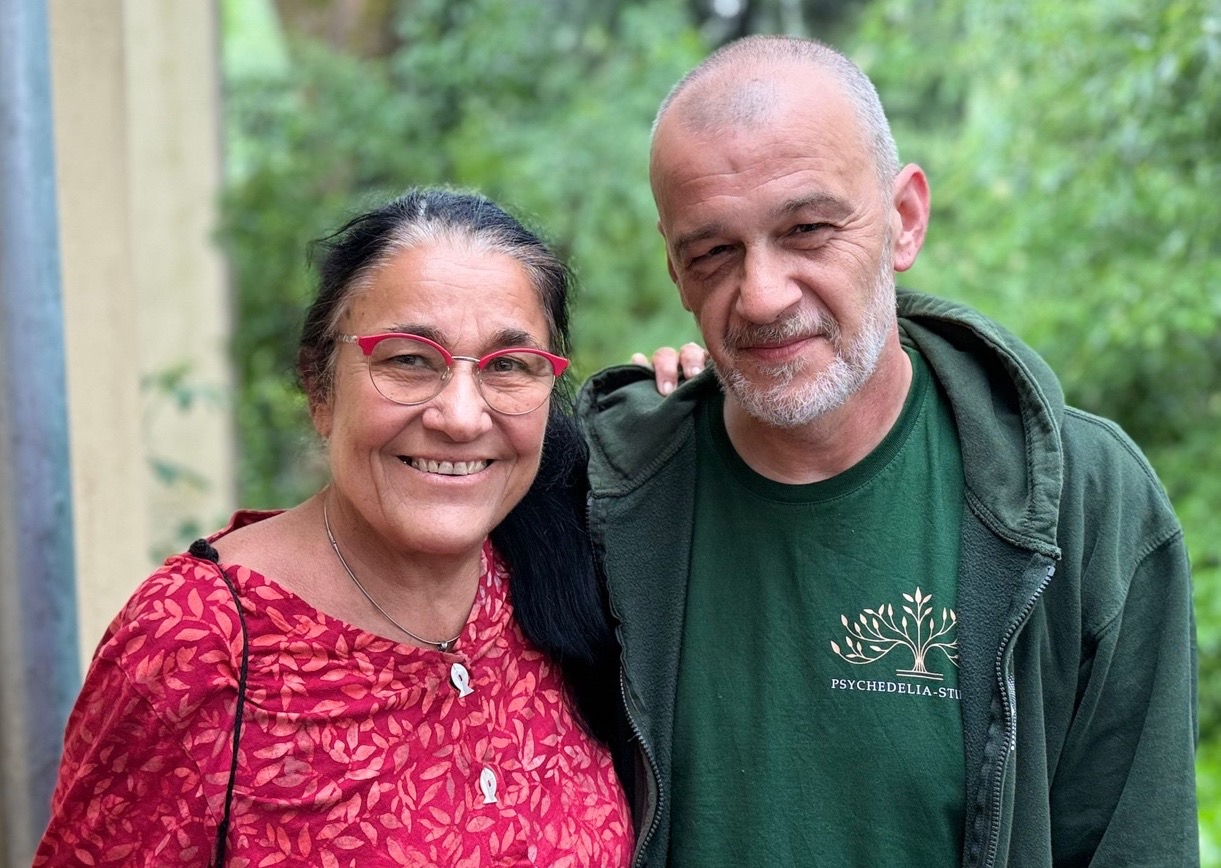 Claudia Müller-Ebeling and Markus Berger, the retreat facilitators, smiling at the camera with green nature in the background.